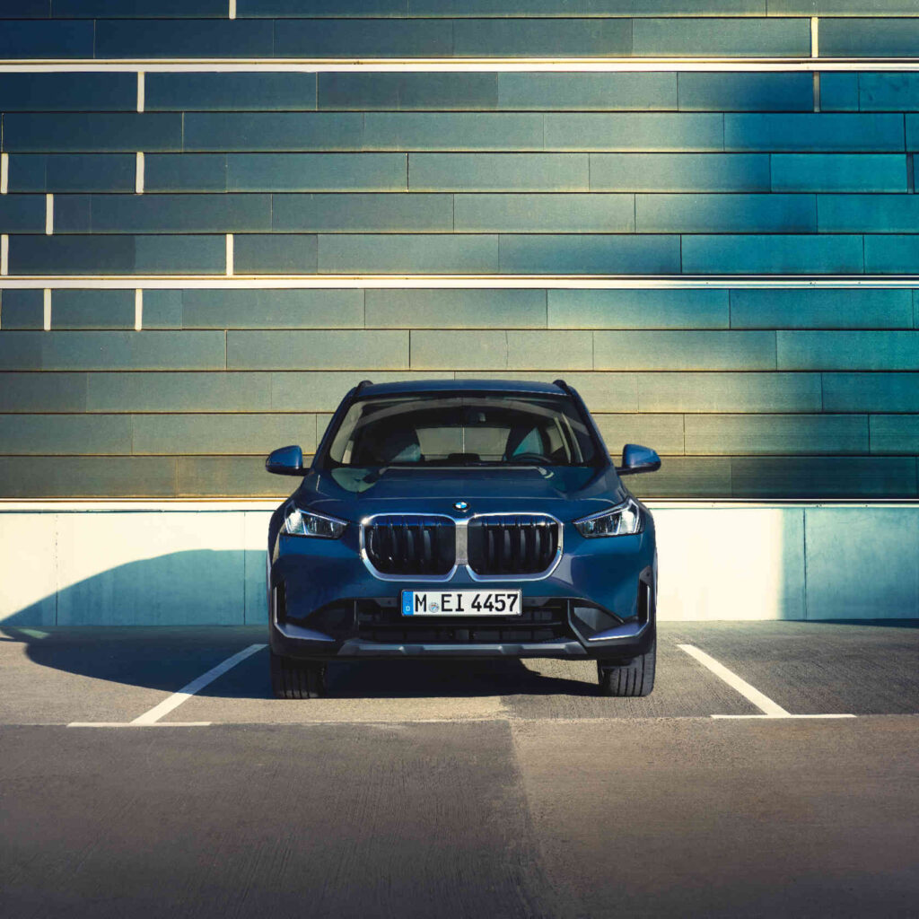 BMW X1 U11 parkt vor blauem modernen haus